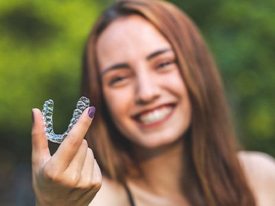 A beautiful, blurred woman holding an Invisalign tray in front of herself