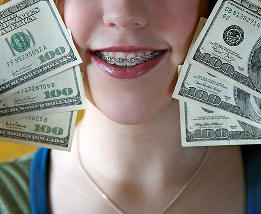 A woman with braces holding hundred-dollar bills next to her face