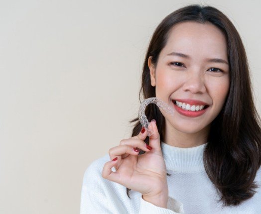 Smiling woman holding Invisalign clear braces tray