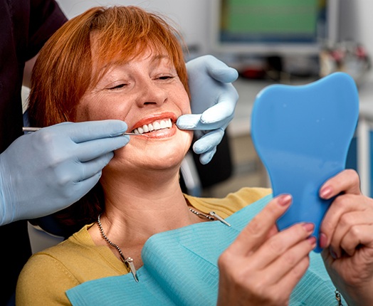 An older woman admiring her dentures with a hand mirror