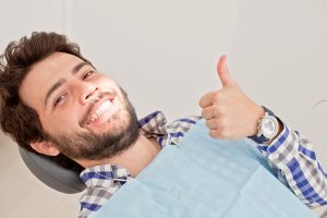 young man smiling sitting in dentist chair after dental checkup