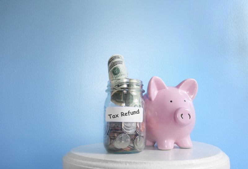 A money jar labelled ‘tax refund’ sitting next to a piggy bank