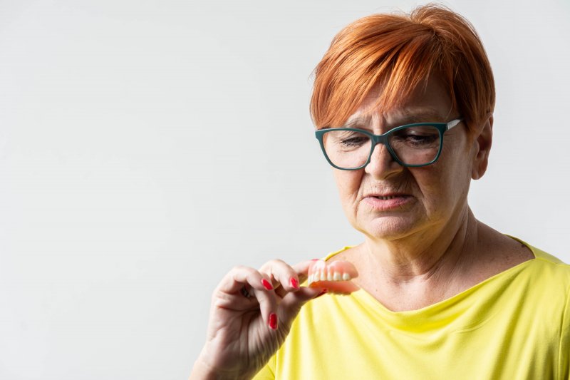 An older woman holding a denture and looking at it skeptically
